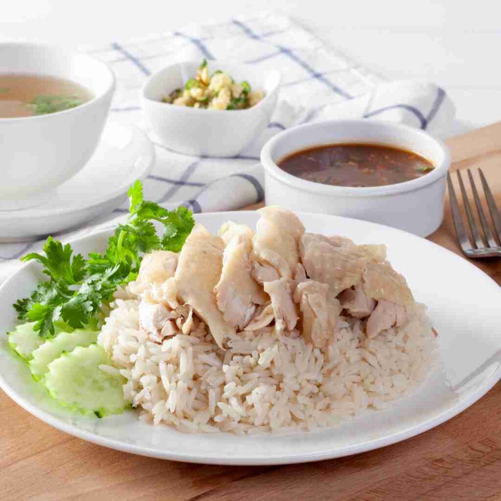 A plate of Halal Khao Man Gai, showing succulent poached chicken over fragrant rice with its signature dipping sauce, a popular Bangkok food dish.
